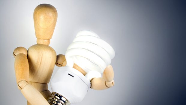 A wooden model grasping a compact fluorescent light bulb.  Great for energy savings or going green concepts.