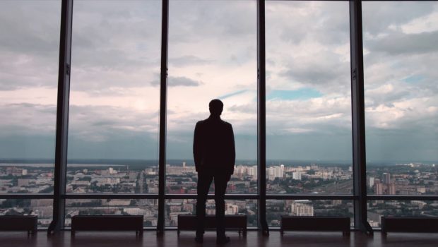 rear-view-of-businessman-in-an-office-with-panoramic-city-view-businessman-admires-the-SBI-351202965