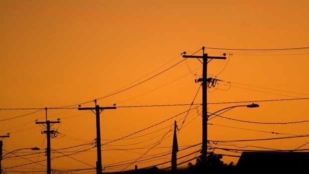 Silhouettes of the power lines and wires in a residential neighborhood backlit by the evening sky.